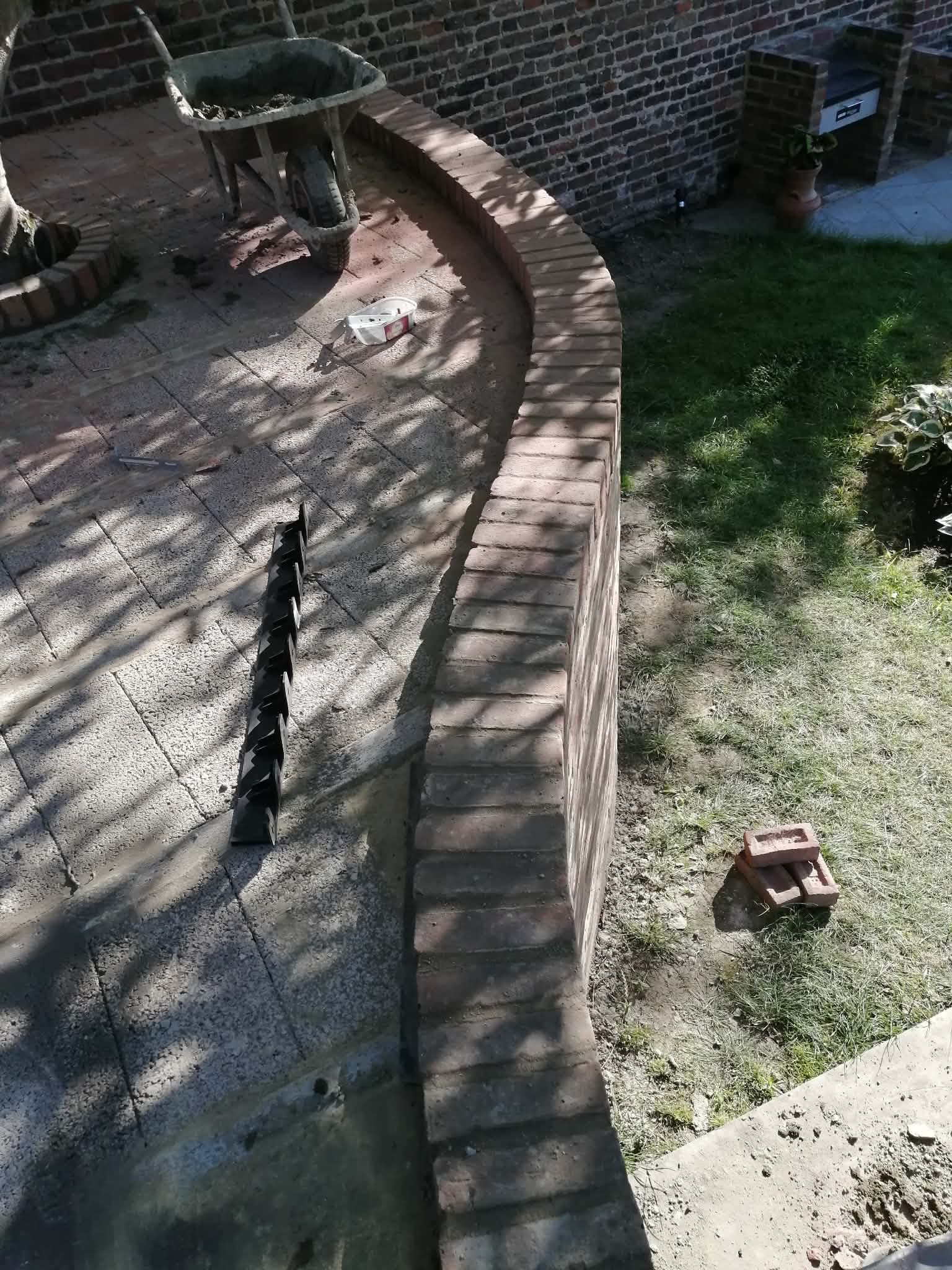 Lenkta raudonų plytų tvora sode
