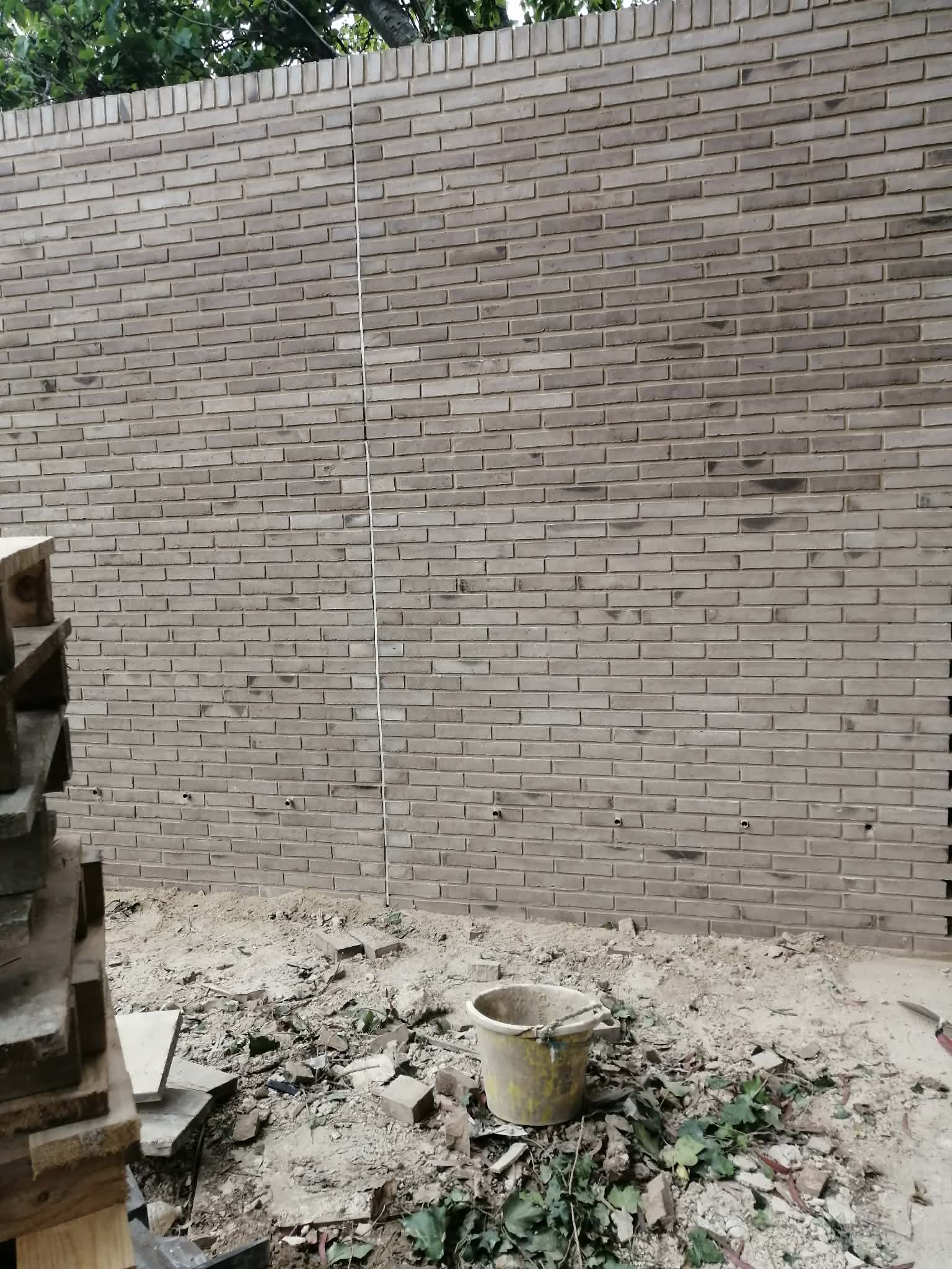 Aukšta pilkų plytų sodo tvora statybos metu